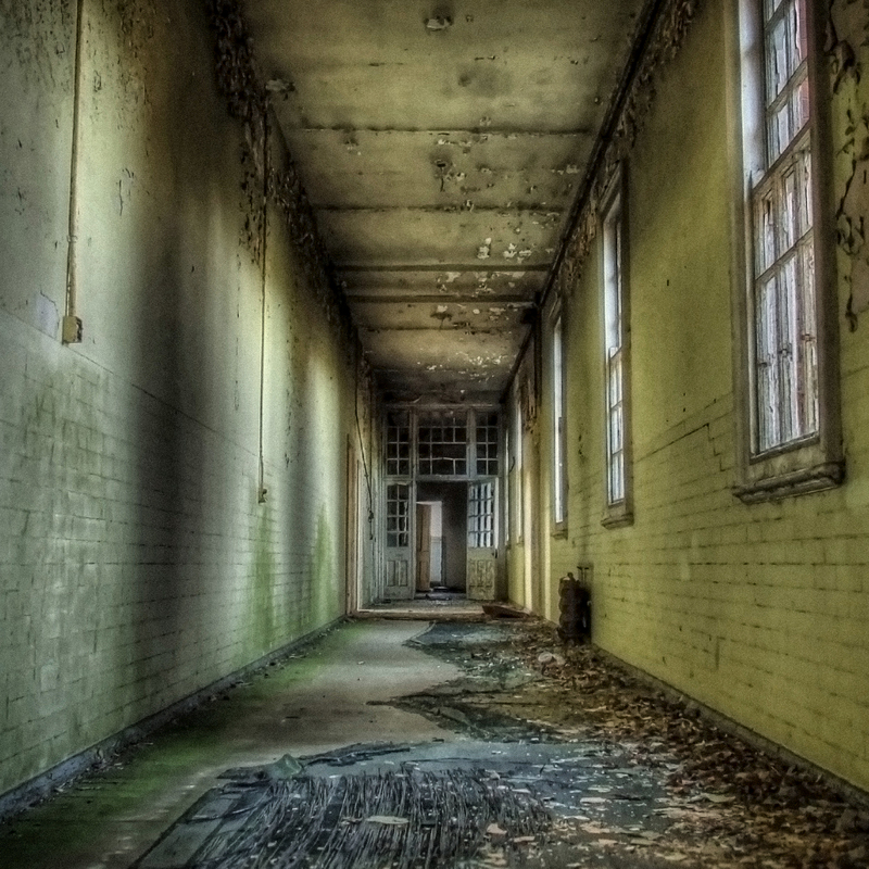 Dark Victorian asylum corridor with shadows highlighting cracked plaster and worn brickwork