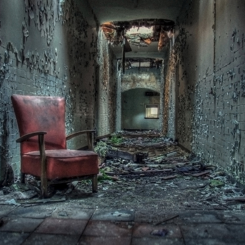Atmospheric photograph of an abandoned lunatic asylum passage with flaking paint and collapsed ceiling plaster